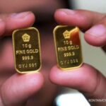 Batangan emas murni yang disusun rapi dengan latar belakang grafik pasar finansial
