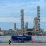 Logo Lotte Chemical dengan latar belakang pabrik petrokimia yang beroperasi