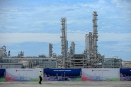Logo Lotte Chemical dengan latar belakang pabrik petrokimia yang beroperasi