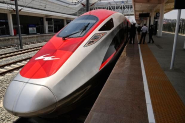 Kereta cepat Whoosh melintas di jalur rel dengan latar belakang pemandangan kawasan urban.